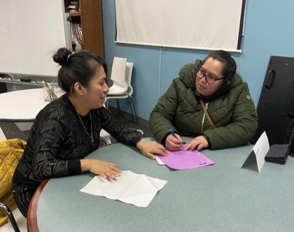 Two women sitting around a table referring to white and pink papers